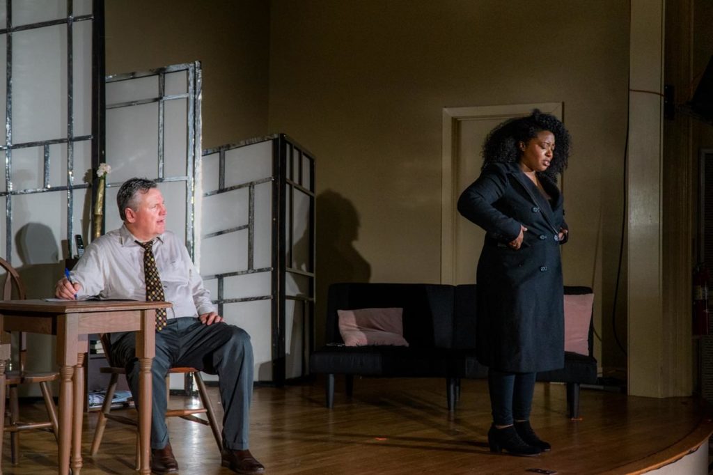 Two actors on a dimly lit sage having what looks like a difficult discussion.